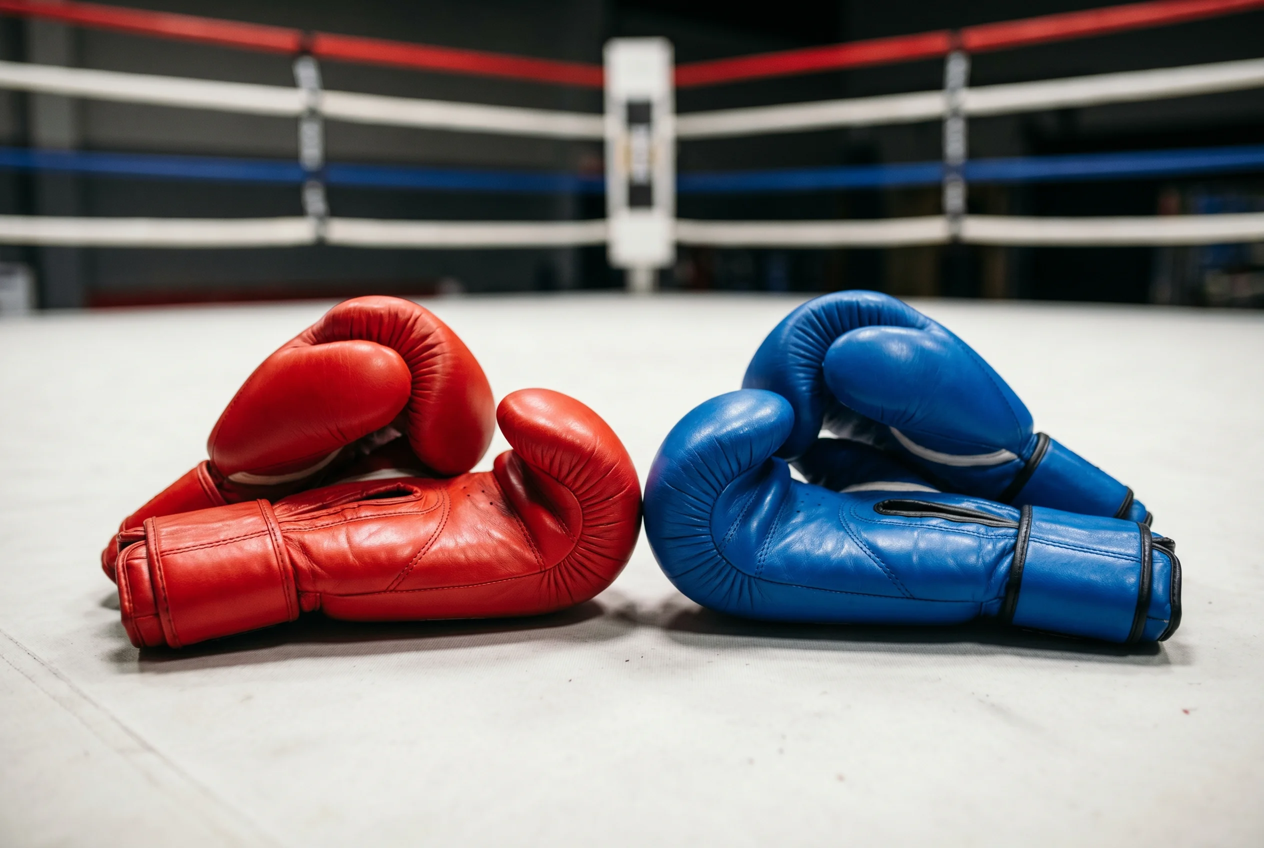 Dos pares de guantes de boxeo rojo y azul colocados enfrentados sobre la lona del ring